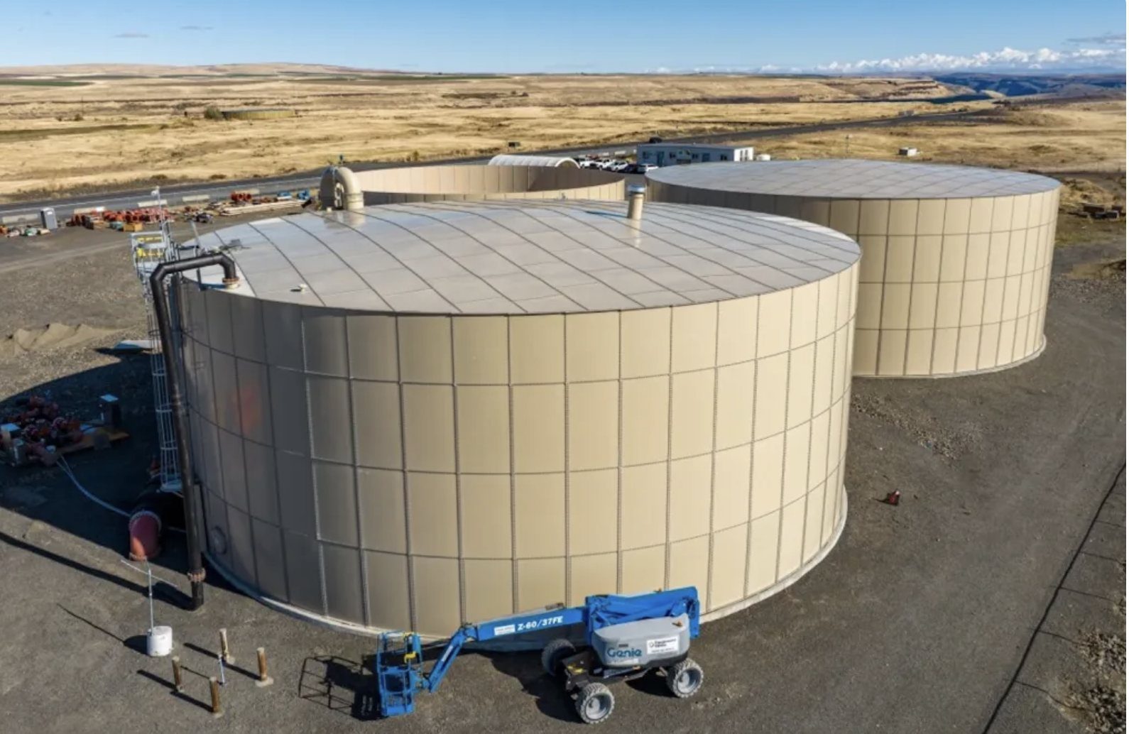 Two bolted steel ground storage tanks with a boom lift beside them